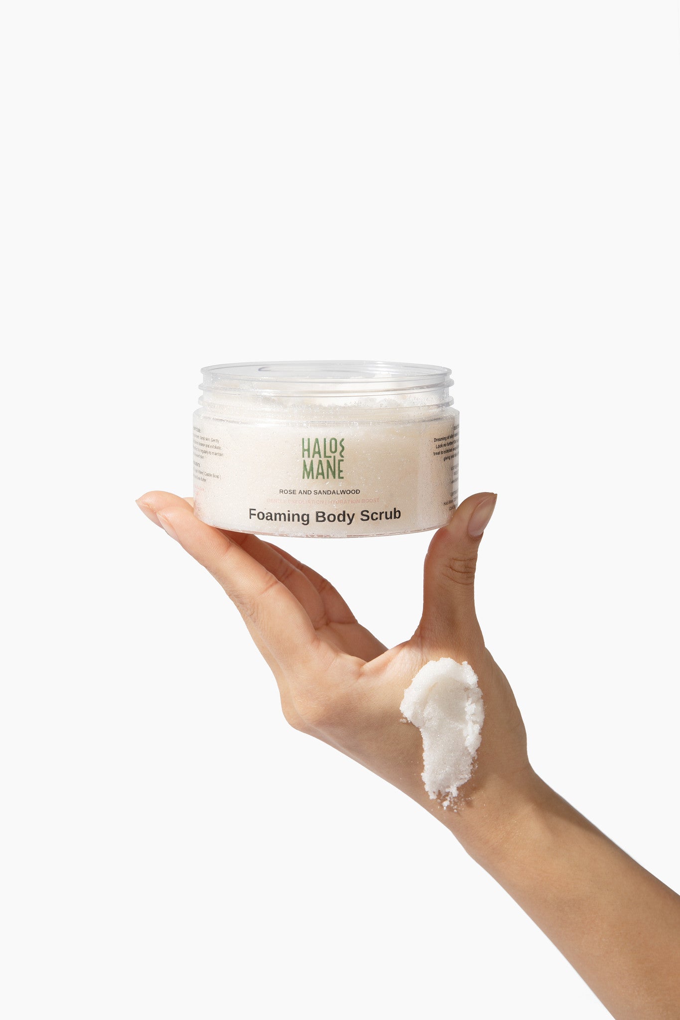 Hand holding a jar of 'Halo mane'  foaming body scrub with a small amount on the palm against a white background